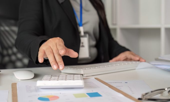 Middle-aged business woman in a modern office, working on paperwork with financial documents and a calculator.